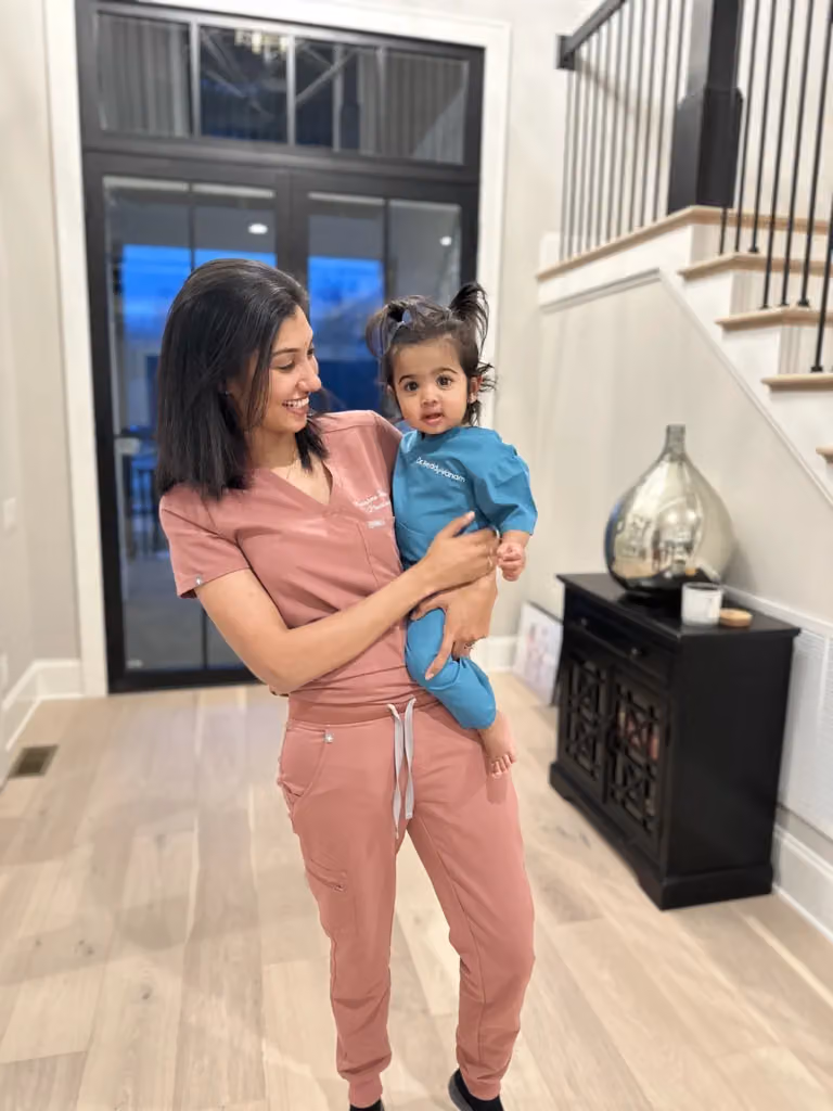 A woman in pink scrubs holding a young child in teal scrubs